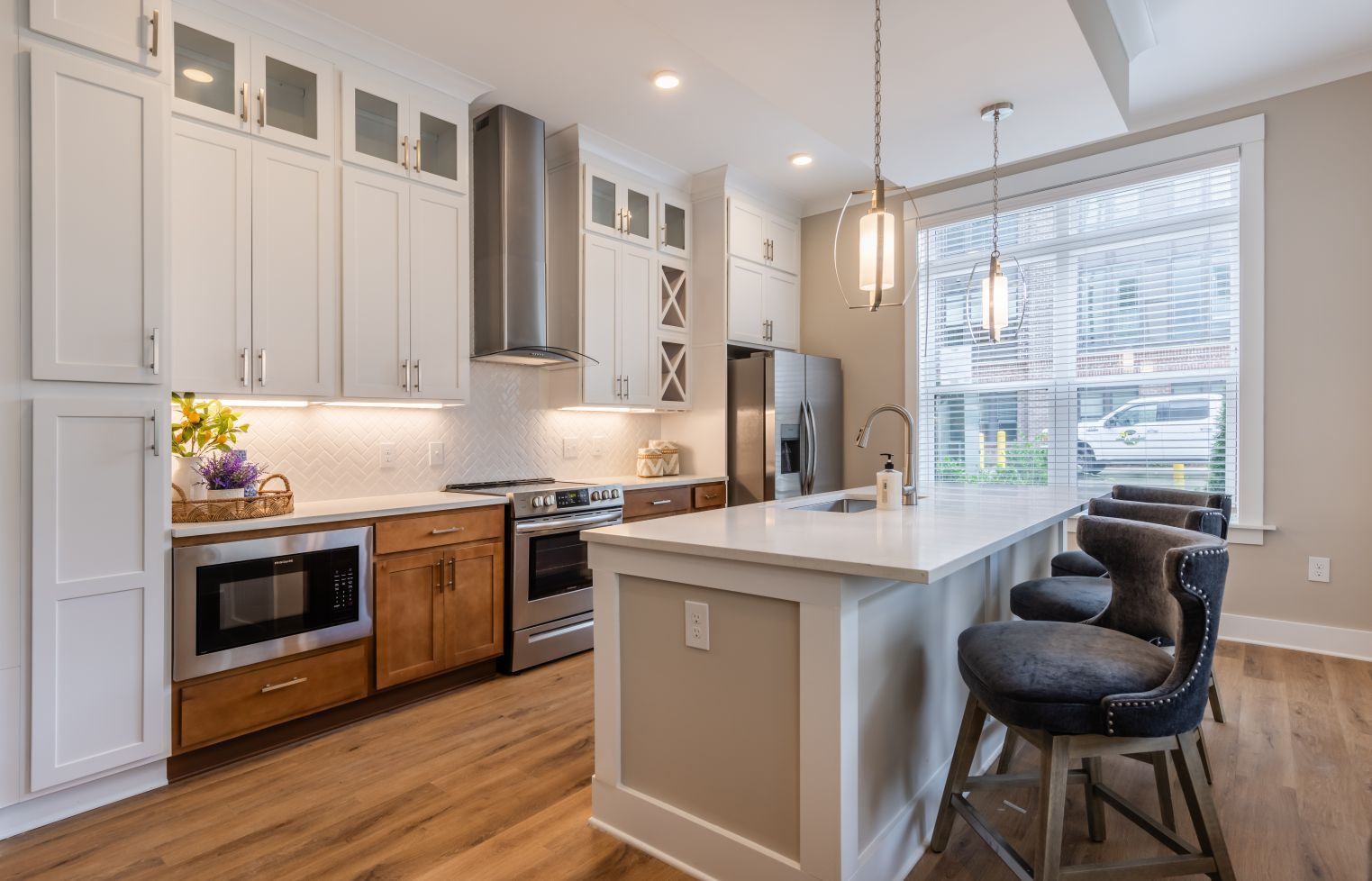 Apartment interior of kitchen with two tone cabinetry, kitchen island, stainless steel appliances, and luxury flooring